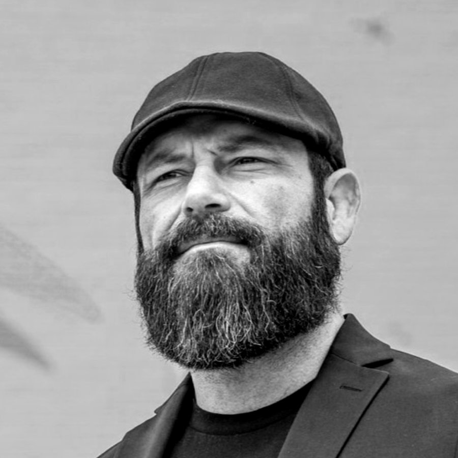 Anthony Canania in a flat cap and blazer, photographed outdoors.