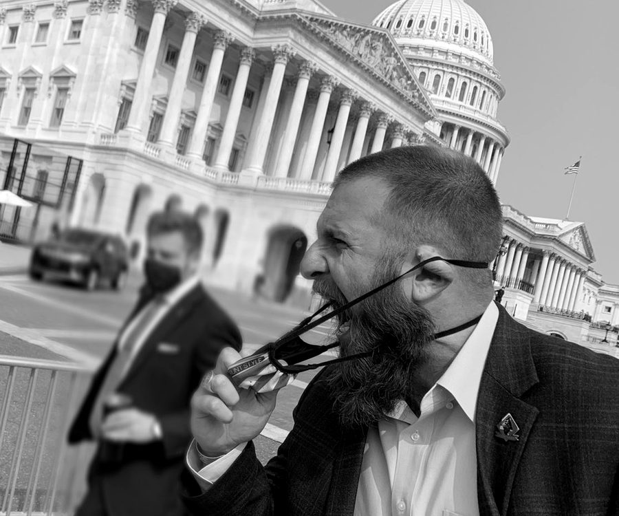 A man in a blazer removing a face covering on the steps outside the United States Capitol.