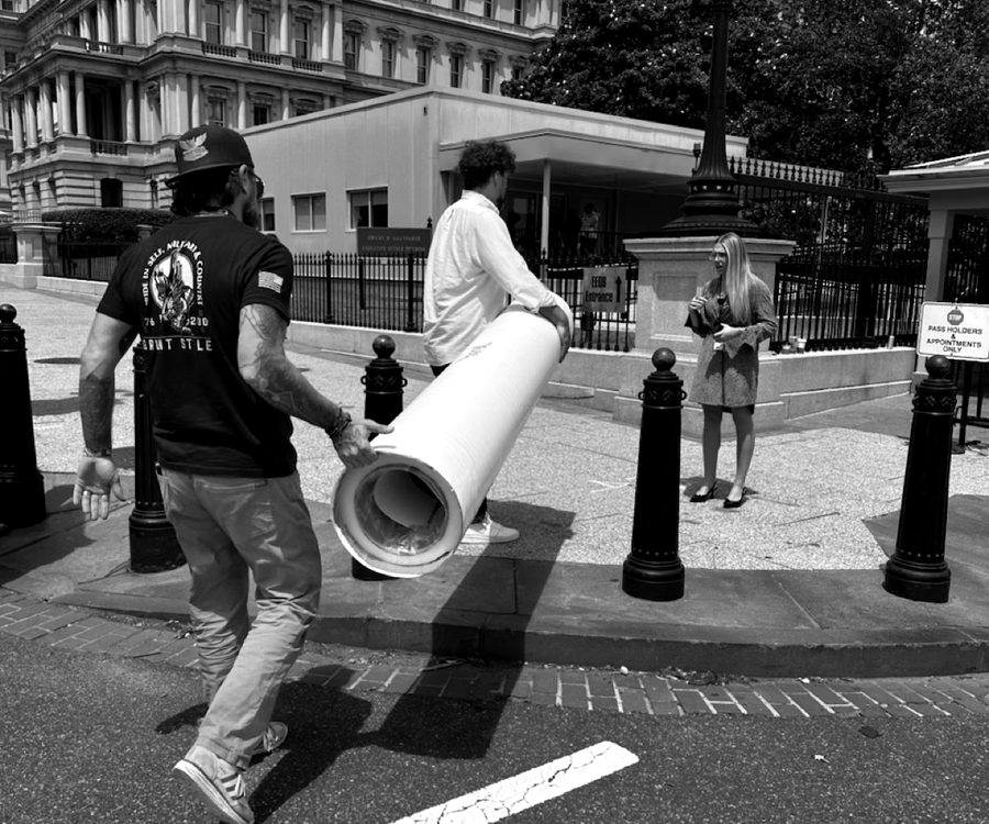 Two men in Grunt Style shirts carrying a large rolled document past the Eisenhower Executive Office Building.