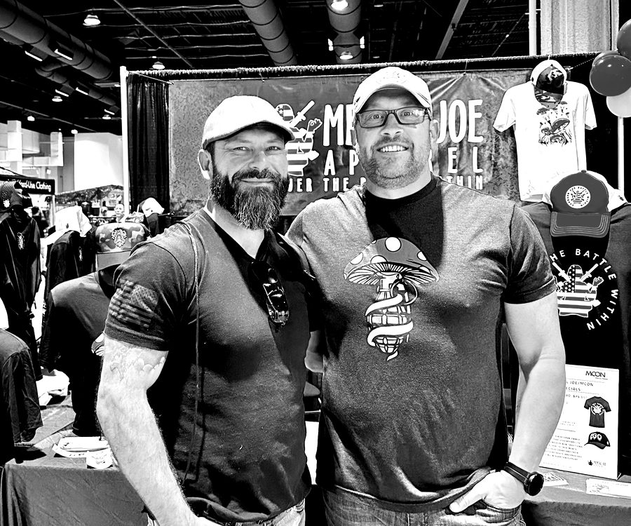 Two men at a veteran apparel booth on a convention floor.