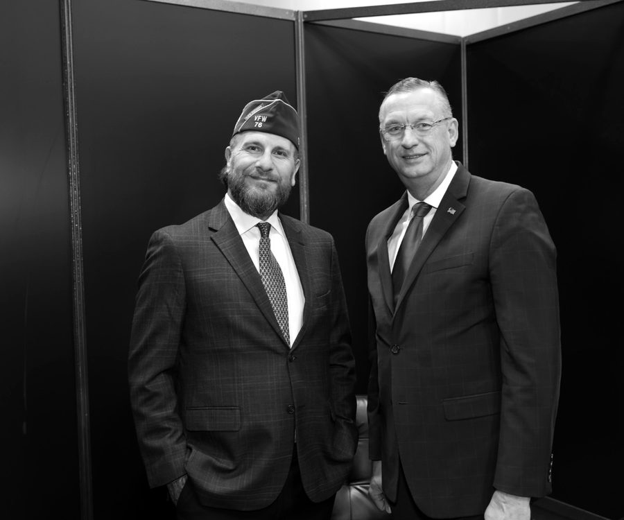 Two men in suits, one wearing a VFW garrison cap, photographed together at an event.