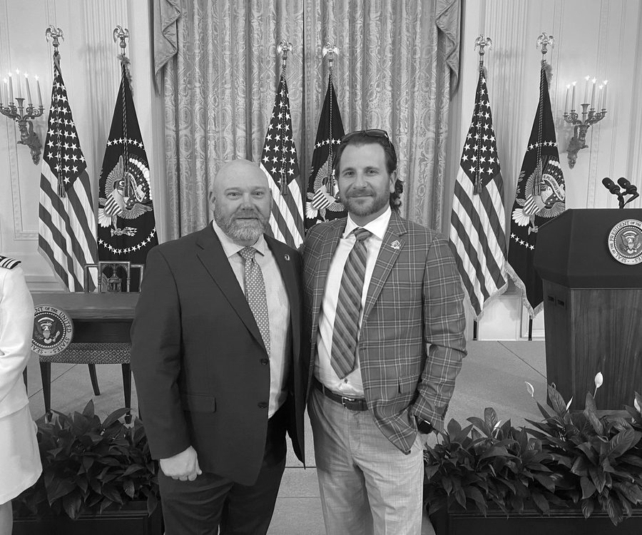 Two men standing before the presidential seal and flags inside the White House.